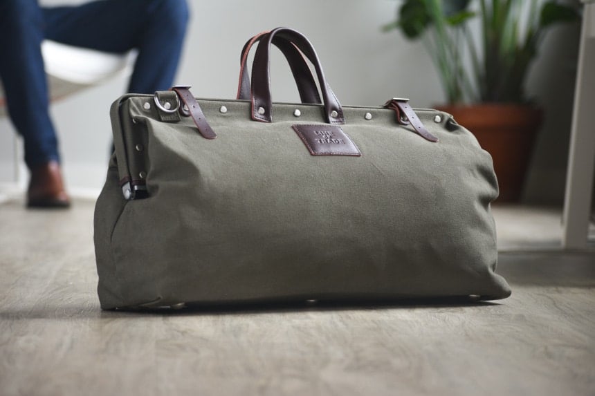 Close Up of Olive Bespoke Post Weekender Bag With Male Model in Background Inside Setting
