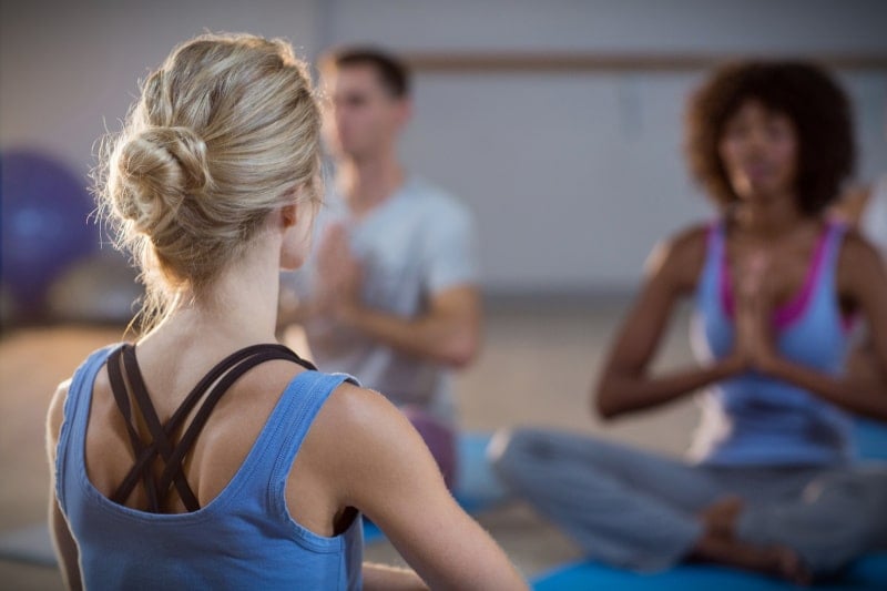 Female instructor teaching yoga class guy and girl