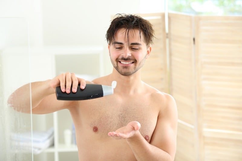 Handsome man with bottle of shampoo taking shower