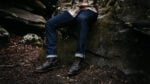 How Should Jeans Fit Model Wearing Outerknown Jeans and boots Sitting on a Rock