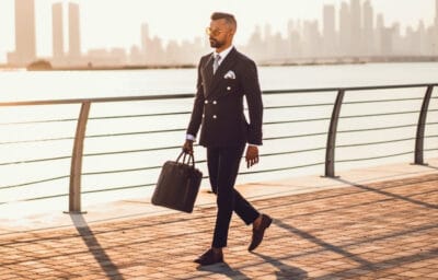 2020/10/How-to-wear-a-gray-suit-with-brown-shoes_-Image-of-model-outside-carrying-briefcase-and-wearing-double-breasted-gray-suit-with-brown-shoes-and-no-socks.jpg