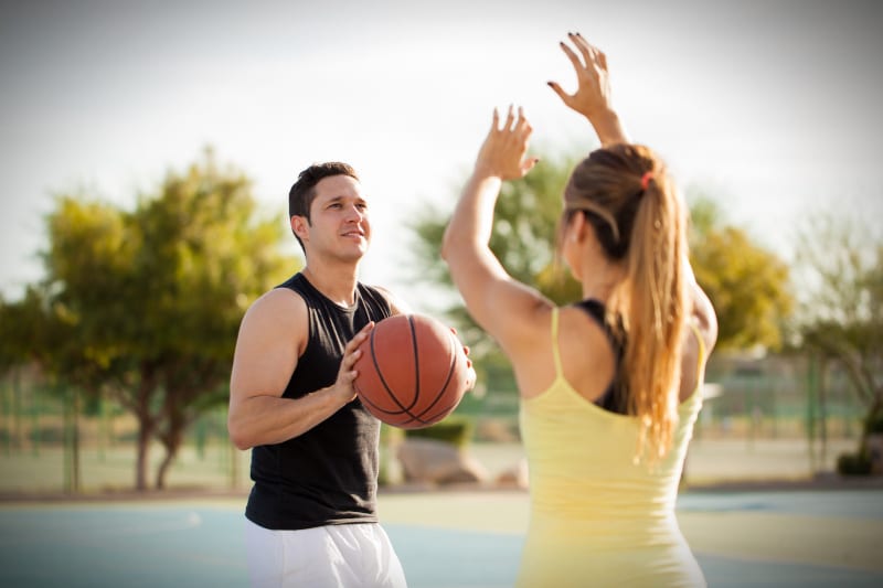 Man playing basketball outside with woman defending
