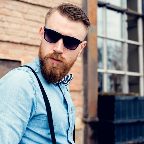 Man with a high fade and an oblong face style wearing sunglasses and with a red beard and suspenders