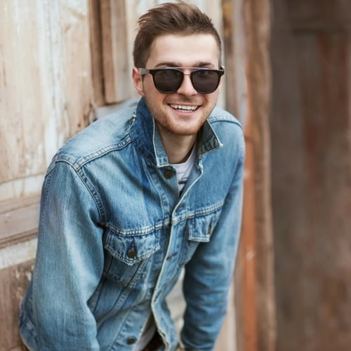 man with round face and close beard with sunglasses on smiling and wearing a jean jacket