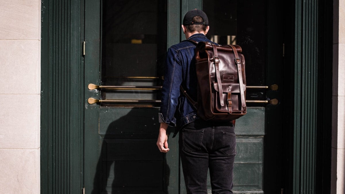 model wearing moral code leather rolltop backpack entering a door