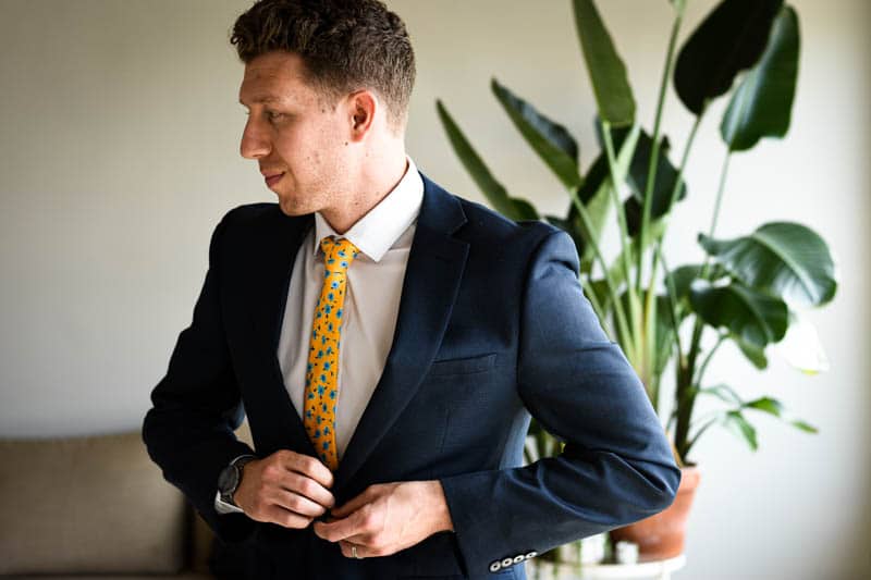 model wearing navy suit white shirt and yellow floral tie