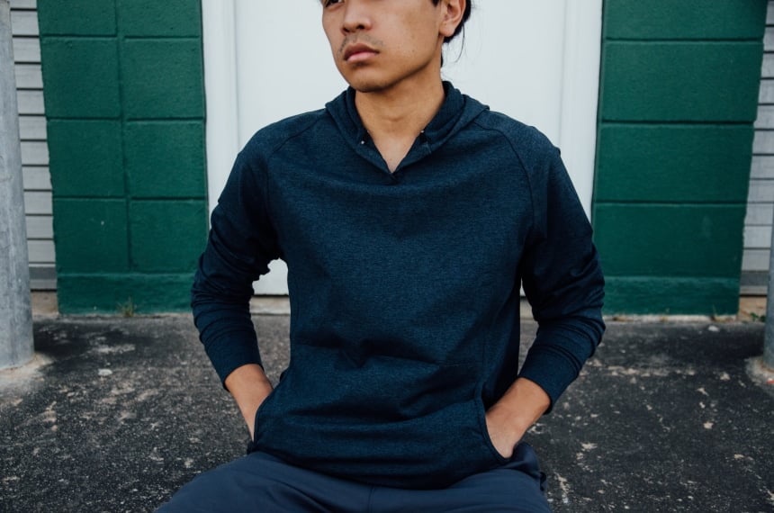 Model Wearing Public Rec Politan Hoodie And Sitting Down With Hands In Pockets