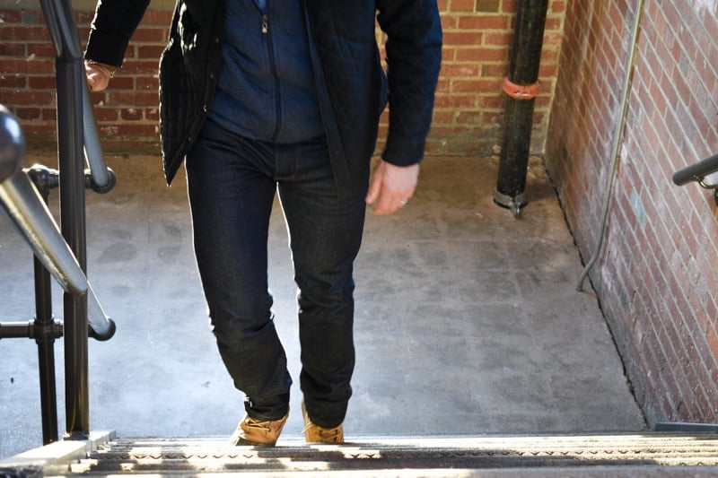 model walking up steps mott and bow jeans blue vest and black coat backlit