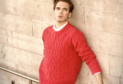 2020/10/Shetland-Sweaters_-Model-Leaning-Against-the-Wall-Wearing-a-Red-Sweater.jpg
