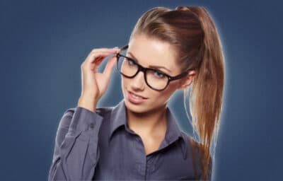 2020/10/Signs-a-Female-Coworker-Likes-You_-Attractive-Woman-With-One-Hand-on-Glasses-Looking-at-Camera-and-Smiling.jpg
